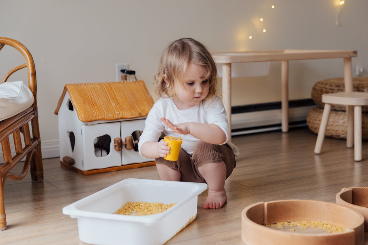 Services A young child playing with macaroni in a cozy indoor playroom setting.
