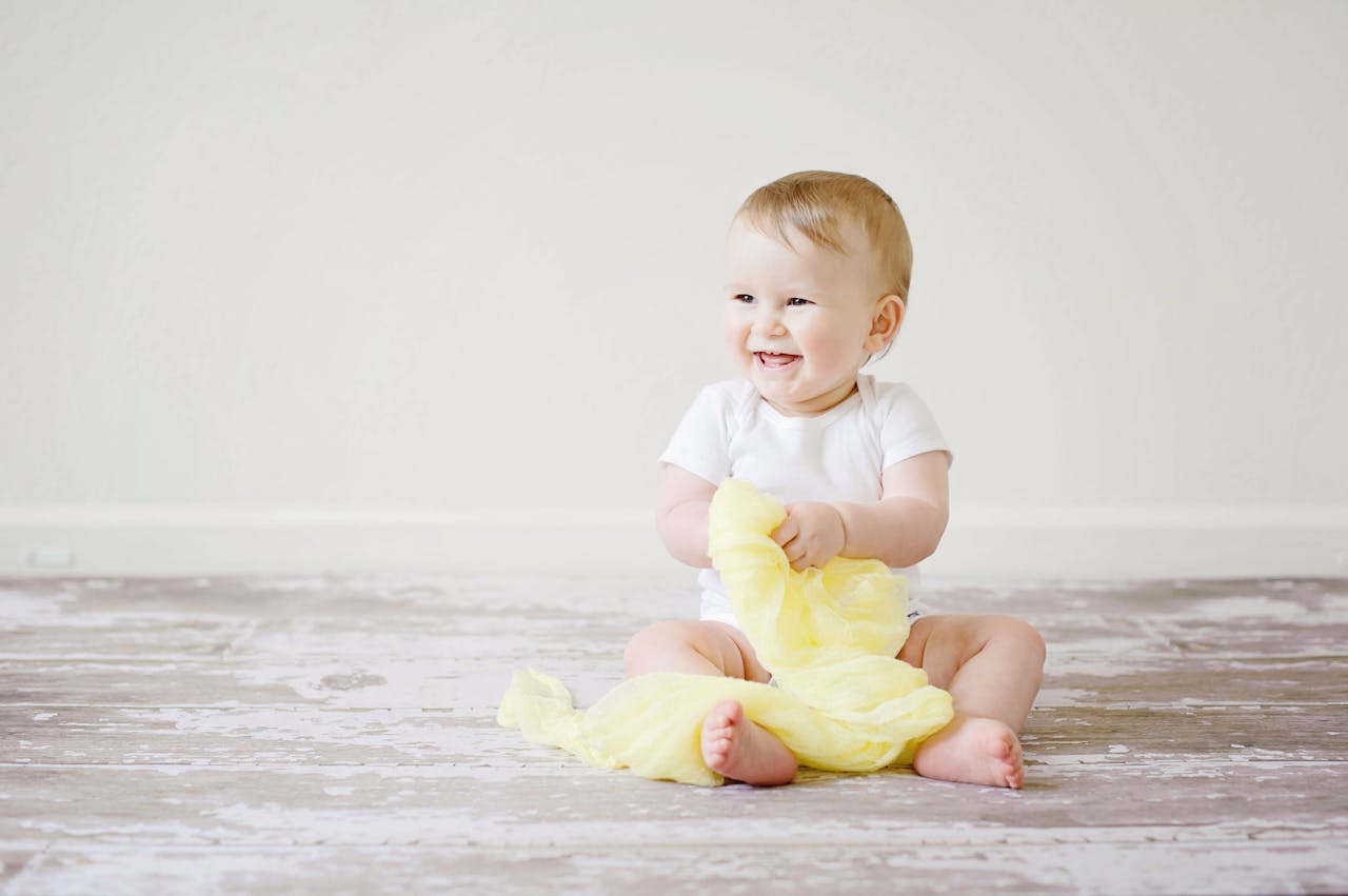 About Adorable baby laughing while sitting on the floor with a yellow blanket indoors, showcasing happiness and innocence.