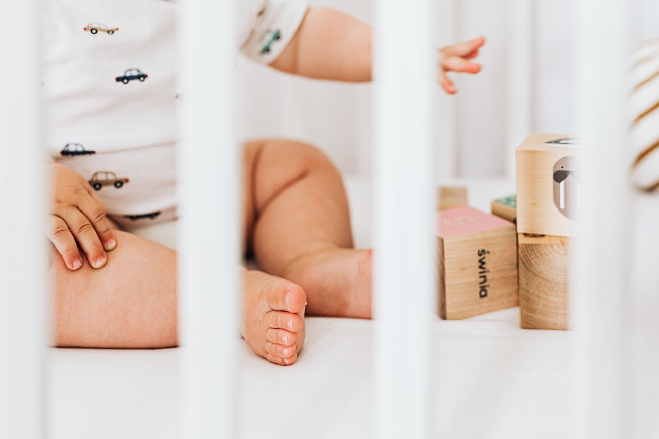 A cute baby sits in a crib playing with colorful wooden blocks, showcasing a peaceful nursery environment.